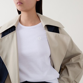 Model wearing Hugo Boss white cotton modal silk top with small logo embroidery, styled with a beige and navy colour-block jacket.