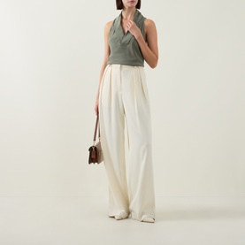 Model wearing Hugo Boss Bolaru Dark Green silk sleeveless blouse with shawl collar, styled with cream wide-leg trousers and brown shoulder bag.