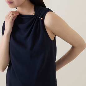 Model wearing Hugo Boss Bannea Draped Top in dark blue, featuring asymmetrical neckline with gold-tone pin hardware and sleeveless design
