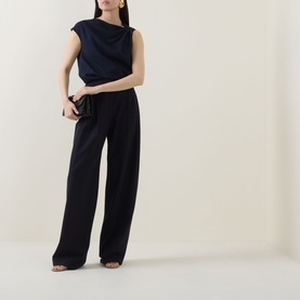 Model wearing Hugo Boss Bannea Draped Top in dark blue with asymmetric neckline, paired with wide-leg black trousers.