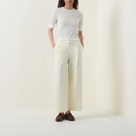 Model wearing Hugo Boss Farbella Knit Top in Open Beige with crew neck and short sleeves, styled with wide-leg cream trousers and brown loafers