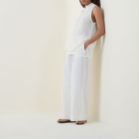 Model wearing Hugo Boss Open White sleeveless cotton top with wide-leg white trousers and tan flat sandals.