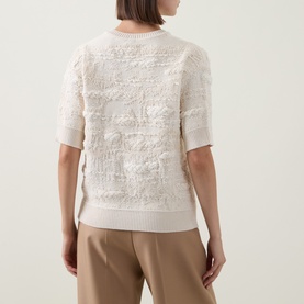 Model wearing Hugo Boss Open White textured knit top with floral appliqu&eacute; detail, short sleeves, styled with beige trousers.