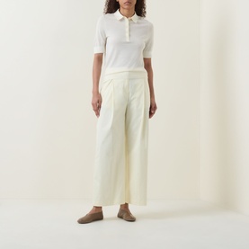 Model wearing Hugo Boss Open Beige virgin wool polo top with short sleeves, styled with cream wide-leg trousers and taupe flats.
