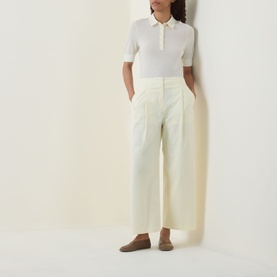Model wearing Hugo Boss Open Beige virgin wool polo top with short sleeves and zip neck, styled with wide-leg cream trousers and taupe loafers.