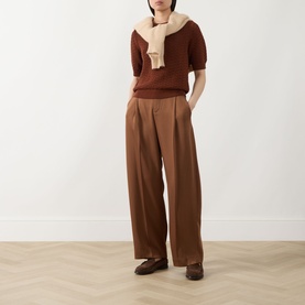 Model wearing Hugo Boss rust/copper short-sleeve knit top with cream scarf, styled with wide-leg brown trousers and loafers.