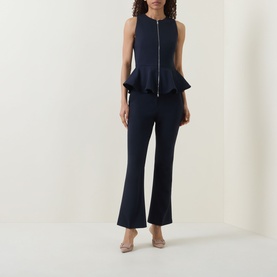 Model wearing navy zip-front sleeveless peplum top with matching navy flared trousers and nude heeled mules