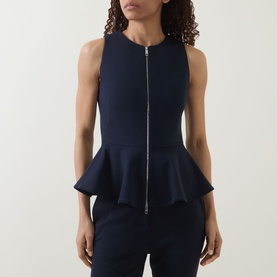 Model wearing navy sleeveless peplum top with front zip fastening, paired with matching navy trousers.