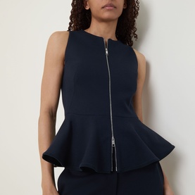 Model wearing navy sleeveless zip-front peplum top with silver zip detail, styled with matching navy skirt.