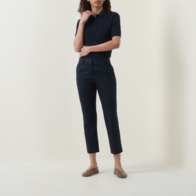 Model wearing navy slim-leg cropped trousers with a matching navy short-sleeve polo top and tan loafers