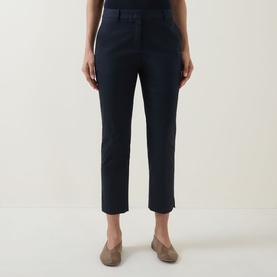 Model wearing navy slim-fit cropped trousers with pressed crease and side slit hem, styled with taupe flat shoes