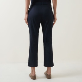 Model wearing navy cropped straight-leg trousers, styled with a black top and beige flat shoes, rear view.