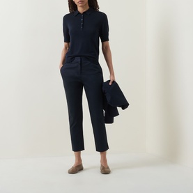 Model wearing navy cropped tailored trousers with matching polo shirt, styled with tan loafers and carrying a navy jacket