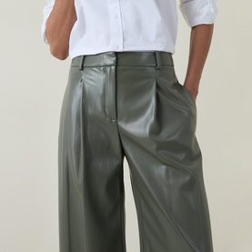 Model wearing Hugo Boss dark green faux leather wide-leg trousers with pleated front, styled with a white shirt.