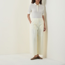 Model wearing Hugo Boss Open Beige cotton-blend trousers with wide-leg silhouette, styled with a white knit polo shirt and tan mules.