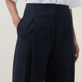 Model wearing Hugo Boss dark blue wide-leg trousers with front pleats and side pockets, styled with a white top.