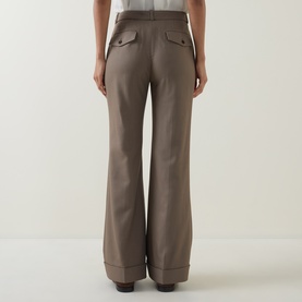 Model wearing Hugo Boss Brown Overflow wide-leg trousers, rear view showing flap pockets and turn-up hems, styled with white top and heels.