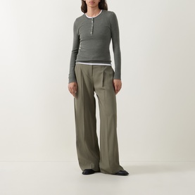 Model wearing Hugo Boss wide-leg trousers in khaki with deep pleats, styled with a striped ribbed henley top and black flat shoes.