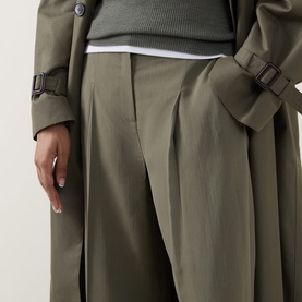 Model wearing Hugo Boss wide-leg tailored trousers in khaki with pleat detail, styled with matching khaki trench coat and grey layered top.