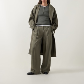 Model wearing Hugo Boss wide-leg trousers in khaki, styled with a matching longline coat and grey ribbed top, black loafers.