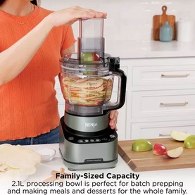 Ninja PrecisionPro Food Processor in silver, shown in use with food inside the 2.1L bowl, held by a model in a kitchen setting.