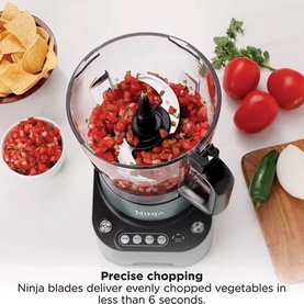 Ninja PrecisionPro Food Processor in silver, shown chopping tomatoes into salsa, with fresh vegetables and tortilla chips alongside