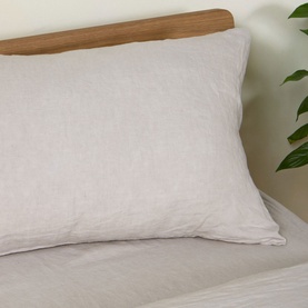 Foxford beige linen pillowcase on a bed with natural wood headboard, styled with a green plant in the background.