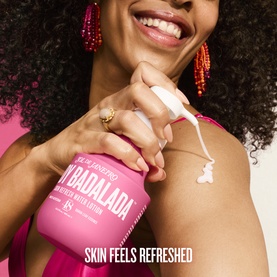 Model wearing pink top applying Sol De Janeiro Badalada body lotion to her arm, with pump bottle visible
