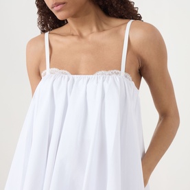 Model wearing Staud Cecily Flared Mini Dress in white, showing lace-trimmed square neckline and thin spaghetti straps