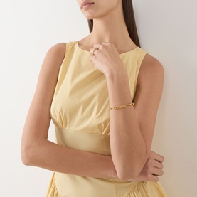 Model wearing Staud butter yellow sleeveless cotton dress, styled with gold chain bracelet and ring.