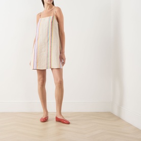 Model wearing Staud dress in Day Trip Stripe, sleeveless mini length with multicolour vertical stripes, styled with red flat shoes