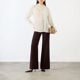 Model wearing Victoria Beckham Elderflower blouse with pintuck detail, styled with dark wide-leg trousers and black kitten heels, carrying a small