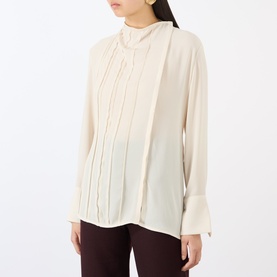 Model wearing Victoria Beckham Blouse in Elderflower, featuring pintuck front detail, ruffle neck, and long flared cuffs, styled with dark trousers.