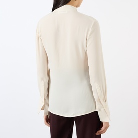 Model wearing Victoria Beckham Blouse in Elderflower, back view showing ruched long sleeves and relaxed fit, styled with burgundy trousers.