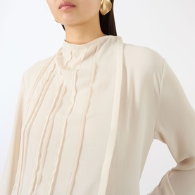 Model wearing Victoria Beckham Elderflower blouse with pleated front detail and high neck, styled with gold drop earrings.