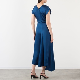 Model wearing Victoria Beckham Aria Twist Waist Dress in Dark Ocean, showing V-shaped back, cap sleeves, and asymmetric midi hem, styled with black