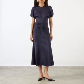 Model wearing Victoria Beckham Midnight dress with puff sleeves, ruched waist detail and midi length, styled with black mules