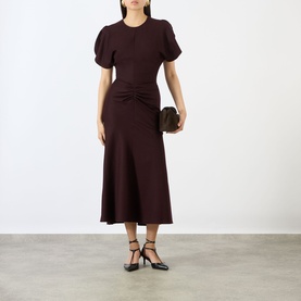 Model wearing Victoria Beckham Dress in Acai, styled with black heeled sandals and a dark clutch bag
