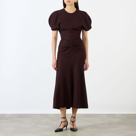 Model wearing Victoria Beckham Acai dress with puff sleeves, ruched waist detail and midi A-line skirt, styled with black strappy heels