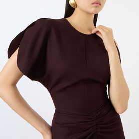 Model wearing Victoria Beckham Dress in Acai, featuring structured puff sleeves and ruched skirt detail, styled with gold earrings
