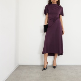 Model wearing Victoria Beckham Gathered Asymmetric Dress in Blackcurrant, midi length with short sleeves and diagonal waist gather, styled with black