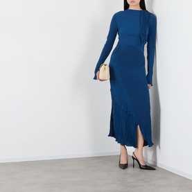 Model wearing blue long-sleeve midi dress with ruffle trim detail, styled with black heels and carrying a small beige shoulder bag