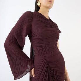 Model wearing Victoria Beckham Dress in Acai, featuring ruched fabric, asymmetric drape, and dramatic flared sleeves, styled with gold earrings