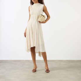 Model wearing Victoria Beckham Pleated Asymmetric Dress in Elderflower, sleeveless midi with high neck and asymmetric hem, styled with a cream mini