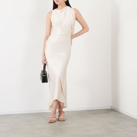 Model wearing a cream sleeveless midi dress with wrap detail and asymmetric hem, styled with nude strappy heels and a black mini bag.