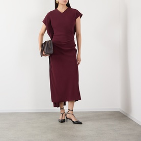 Model wearing Victoria Beckham Victoria Draped Dress in Cinnabar Red, midi length with draped silhouette and asymmetric hem, styled with black heels