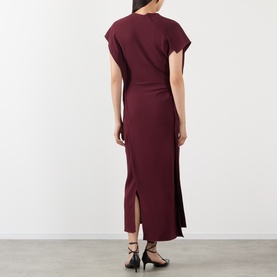 Model wearing Victoria Beckham Victoria Draped Dress in Cinnabar Red, showing rear vent, midi length, and draped silhouette with black strappy heels