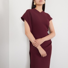 Model wearing Victoria Beckham Victoria Draped Dress in Cinnabar Red, with asymmetric neckline, cap sleeves and draped midi silhouette. Gold hoop