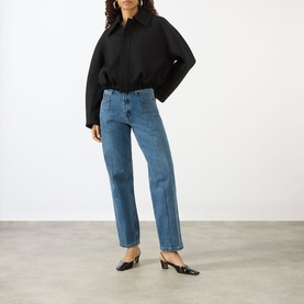 Model wearing Victoria Beckham black oversized jacket with blue straight-leg jeans and black heeled mules.