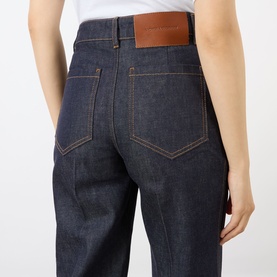 Model wearing Victoria Beckham Alina High-Rise Flared Leg Jeans in indigo with tobacco stitching and brown leather branded patch, rear view